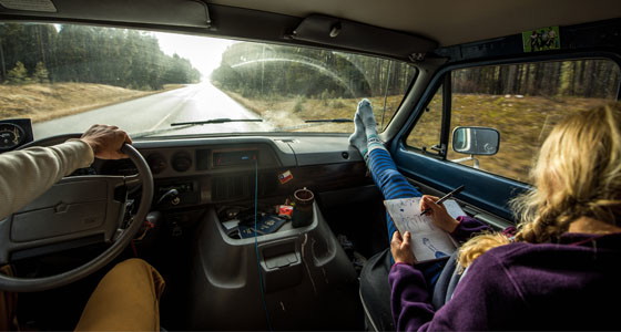 Two people driving a car with one person with their feet up looking at a map wearing Patagonia Clothing.