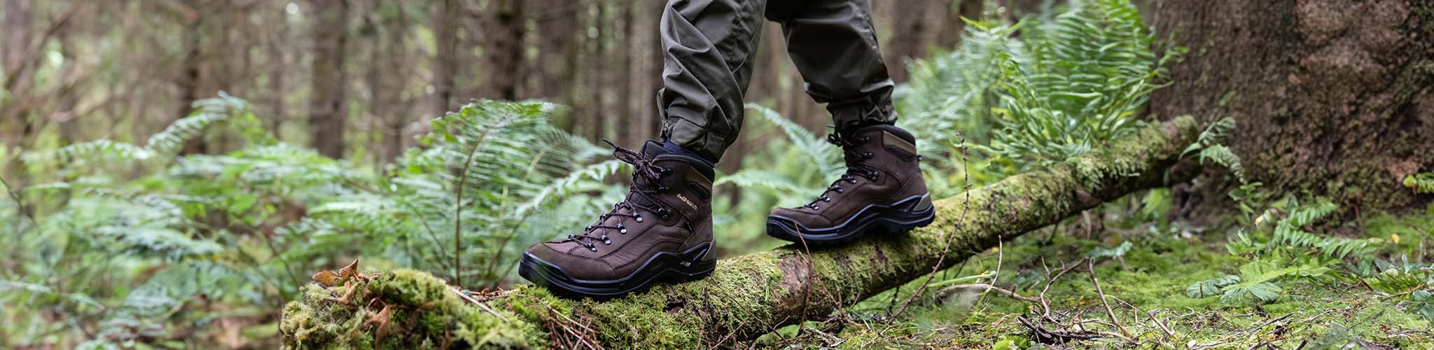 Person's feet are standing on a fallen tree, wearing walking boots
